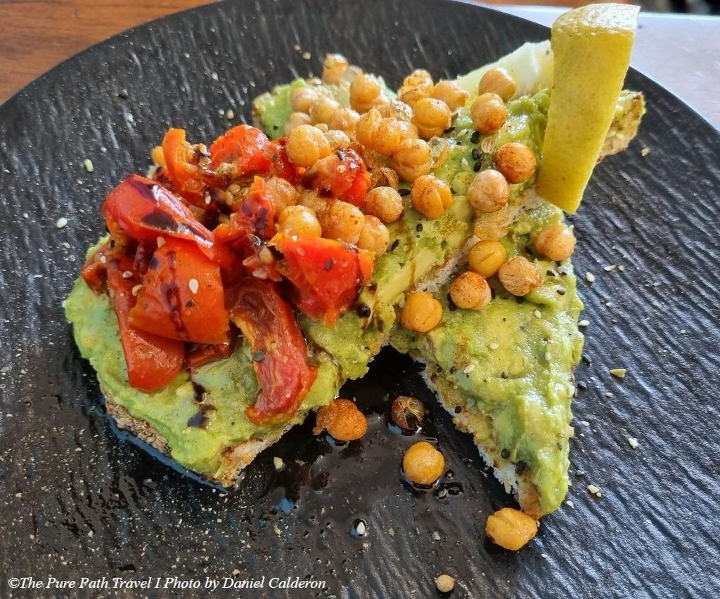 A bright top-down shot of a vibrant, skin-friendly vegan avocado toast seasoned with fresh greens and seeds, served on a rustic plate at Gnostic Mana Cafe in Woy Woy.